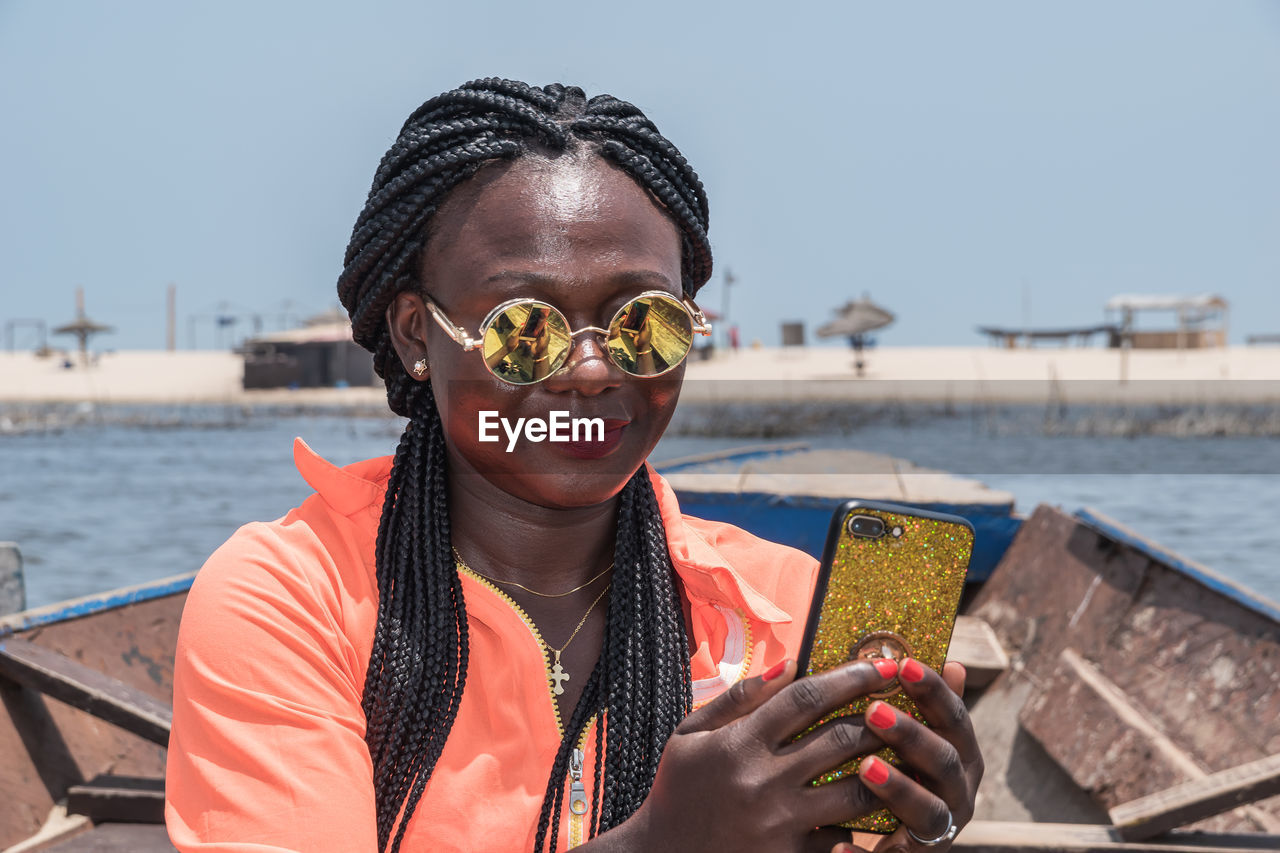 African woman sitting on a boat with mobile phone in hand and taking photos