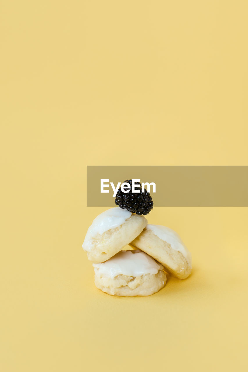 Delicious lemon iced cookies stacked with a blackberry on top on yellow backdrop