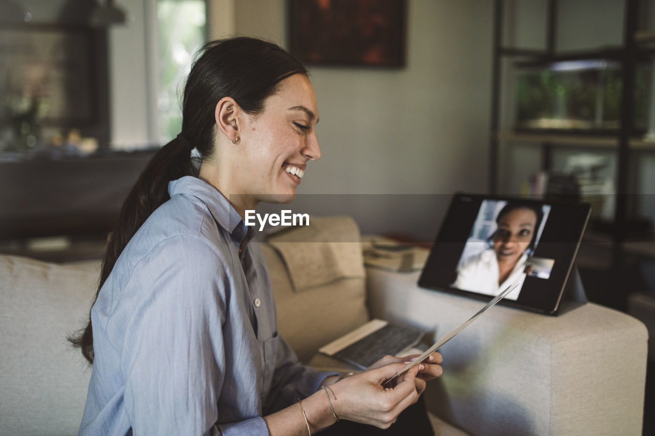 Smiling female entrepreneur with fabric swatch talking through laptop on video conference while working at home