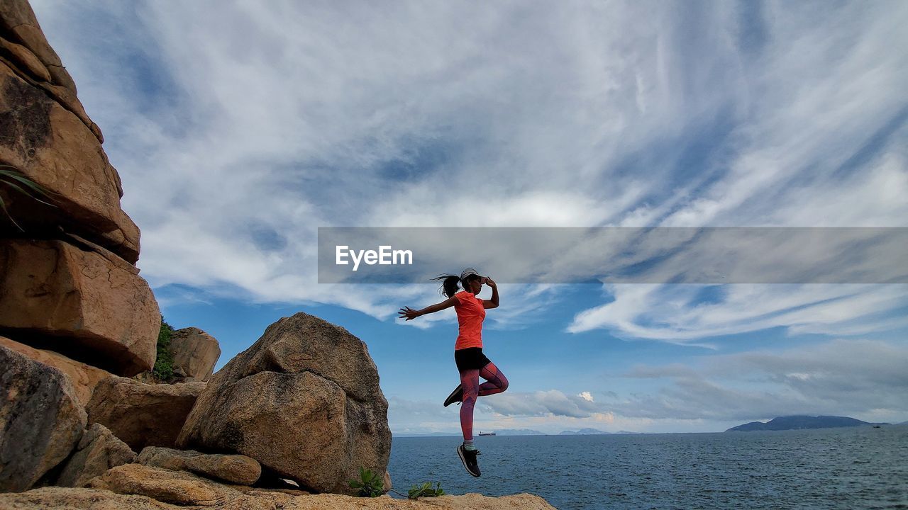 Woman jumping on rock against sea and sky