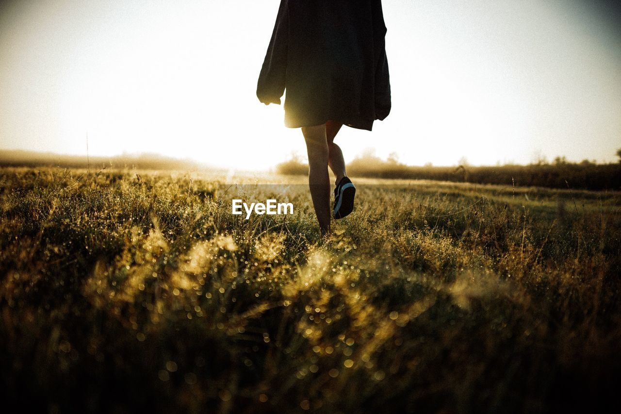 Low section of woman walking on field against clear sky during sunset