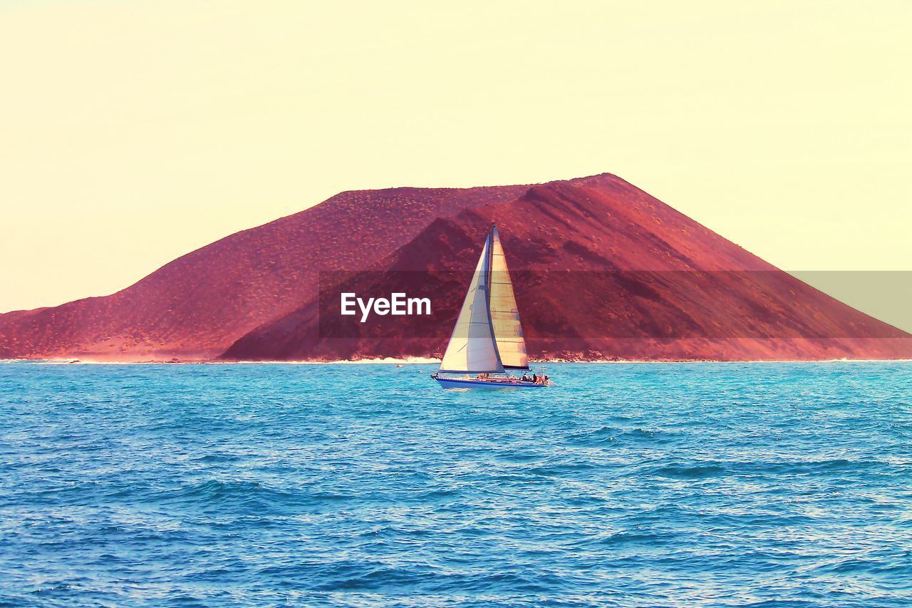 Sailboat sailing on sea against mountain