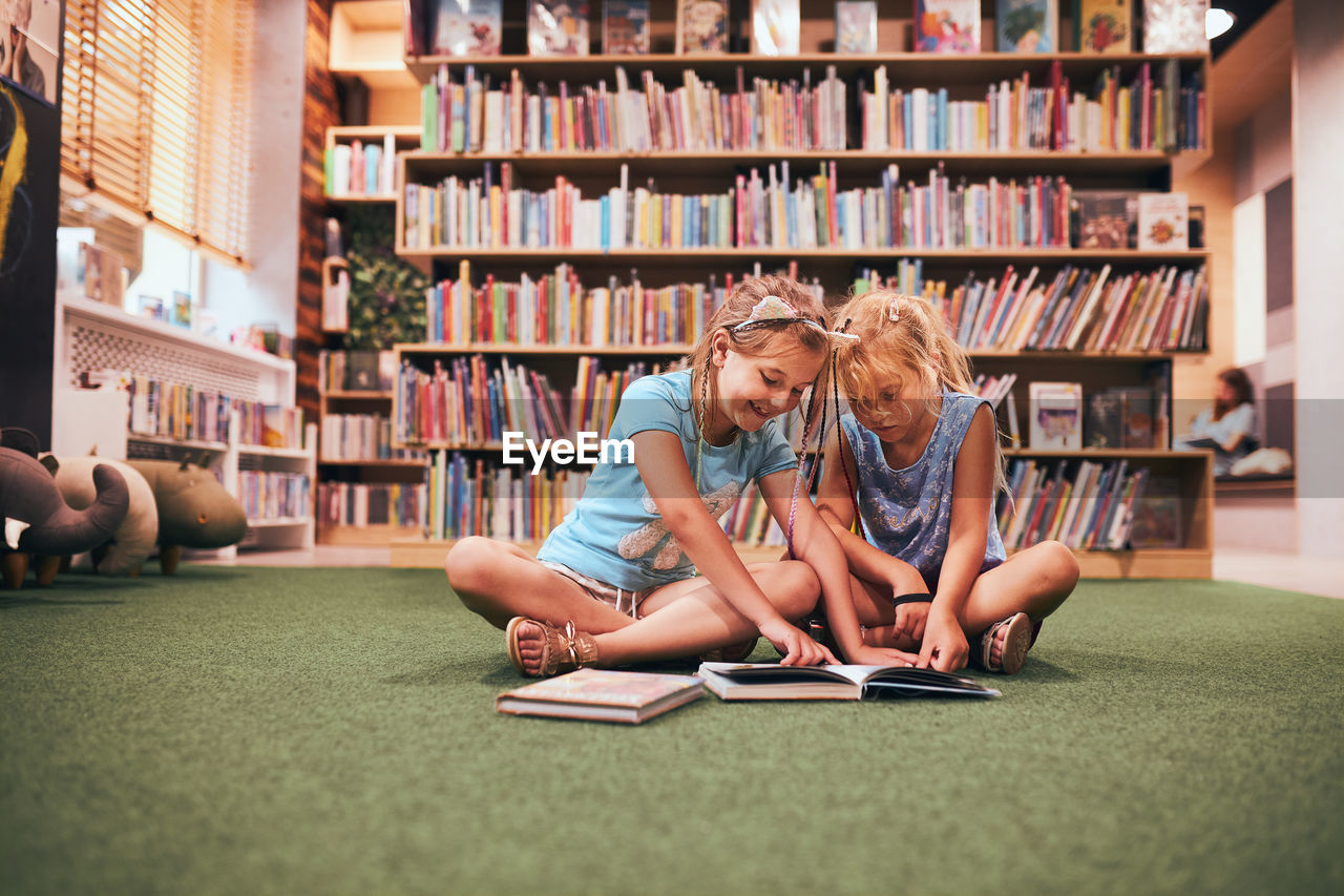 Two primary schoolgirls doing homework in school library. learning from books. back to school