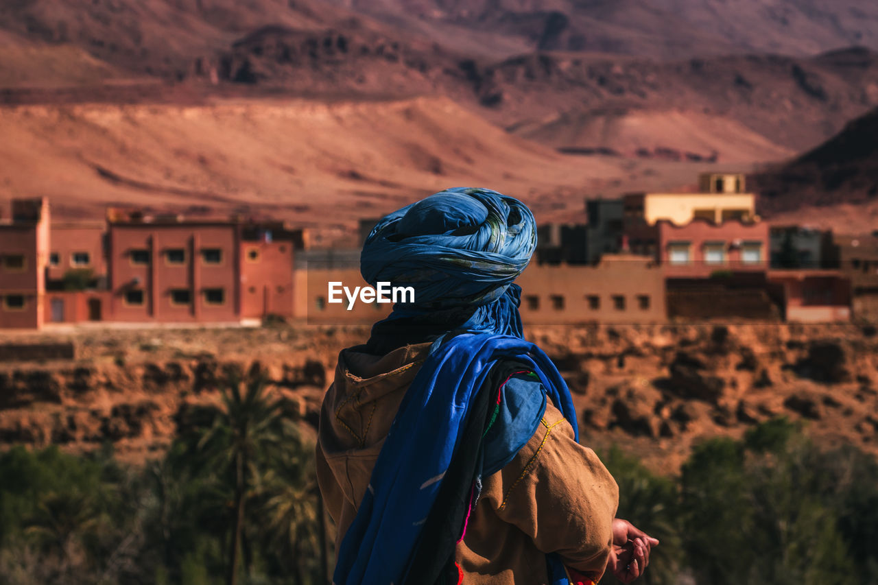 REAR VIEW OF WOMAN STANDING ON MOUNTAIN AGAINST BLURRED BACKGROUND