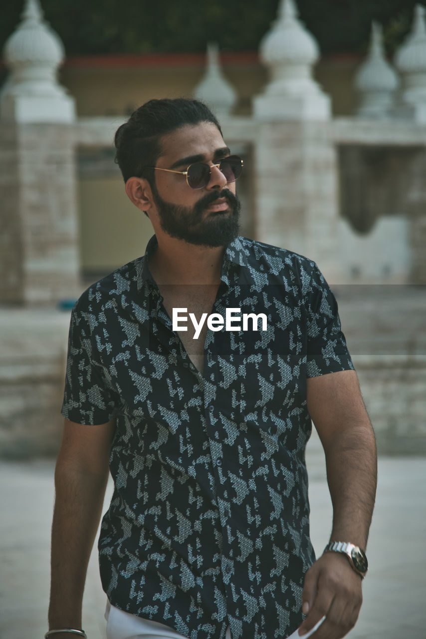 Young man wearing sunglasses standing against built structure