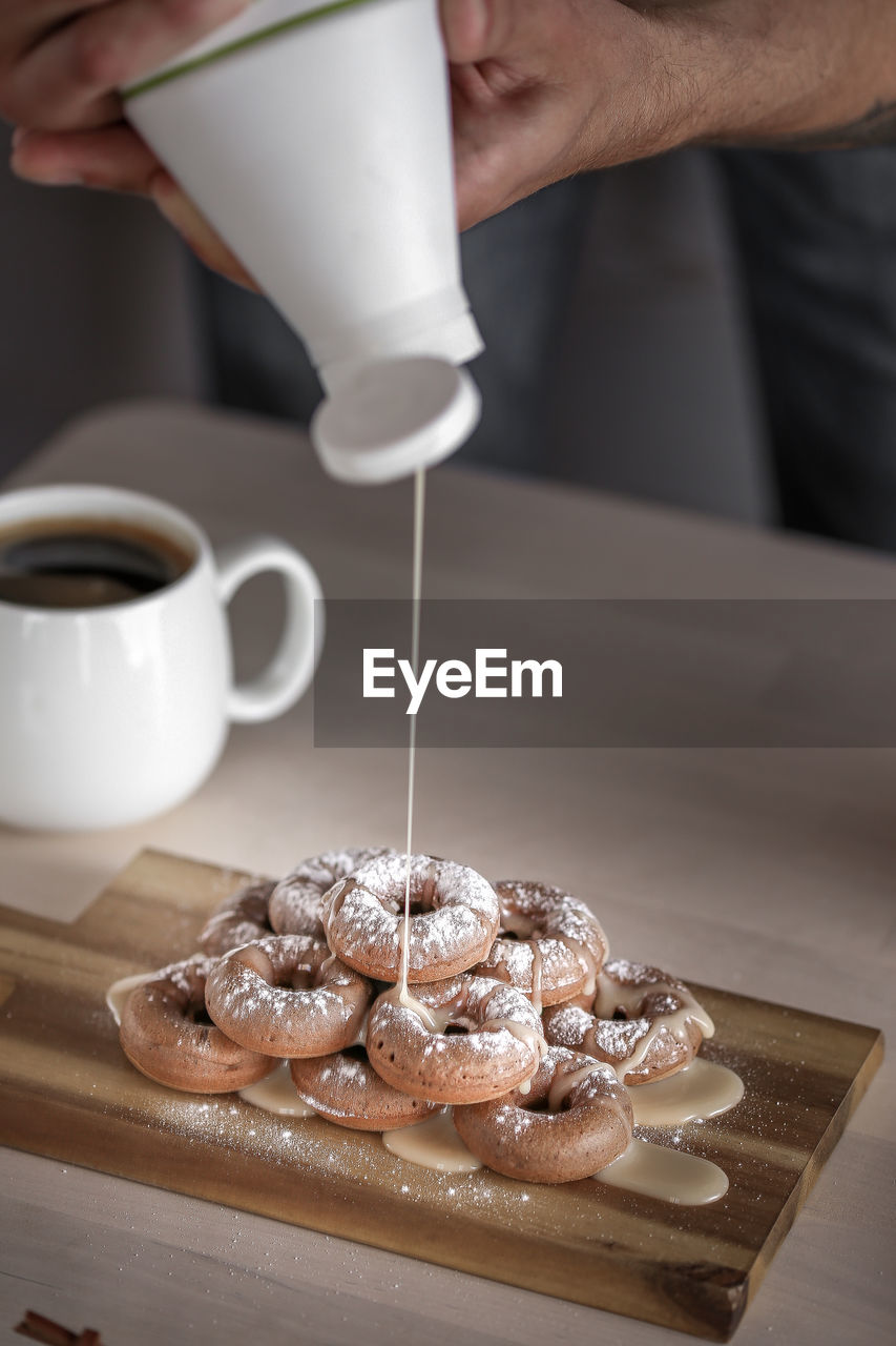 Cropped image of man pouring caramel on donuts in kitchen