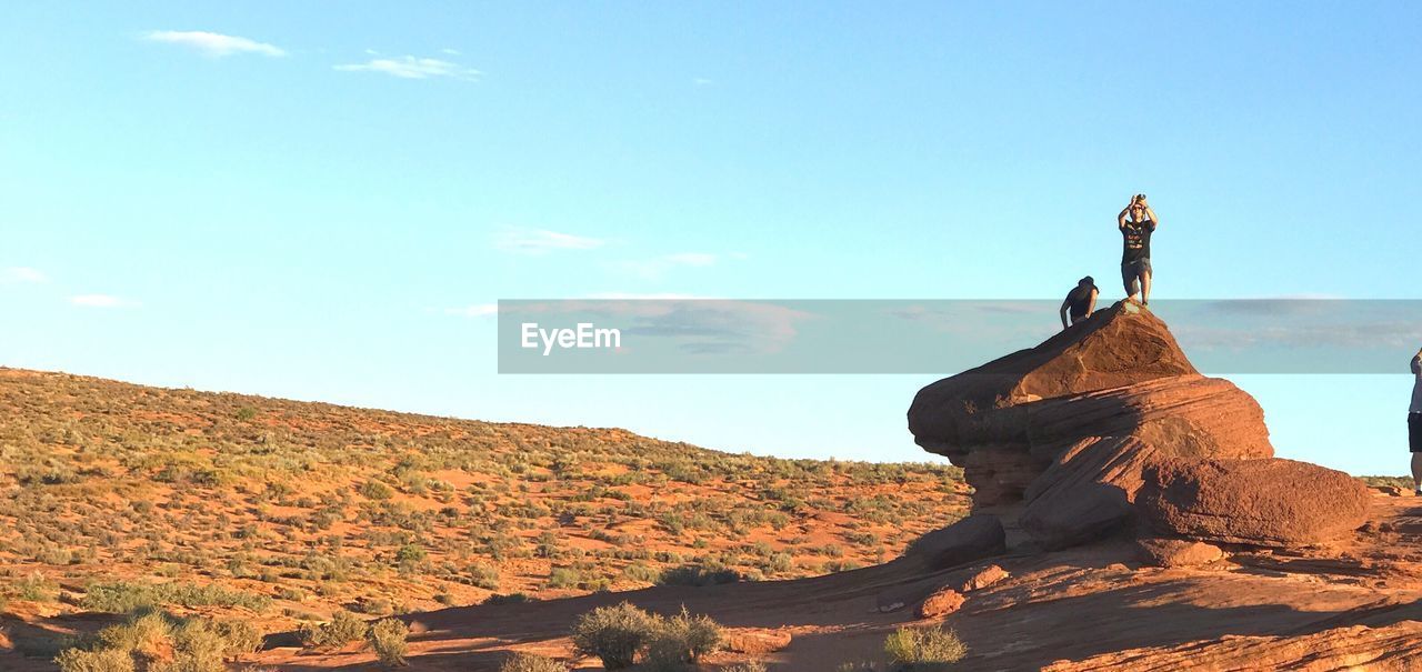 People on rock at desert against sky