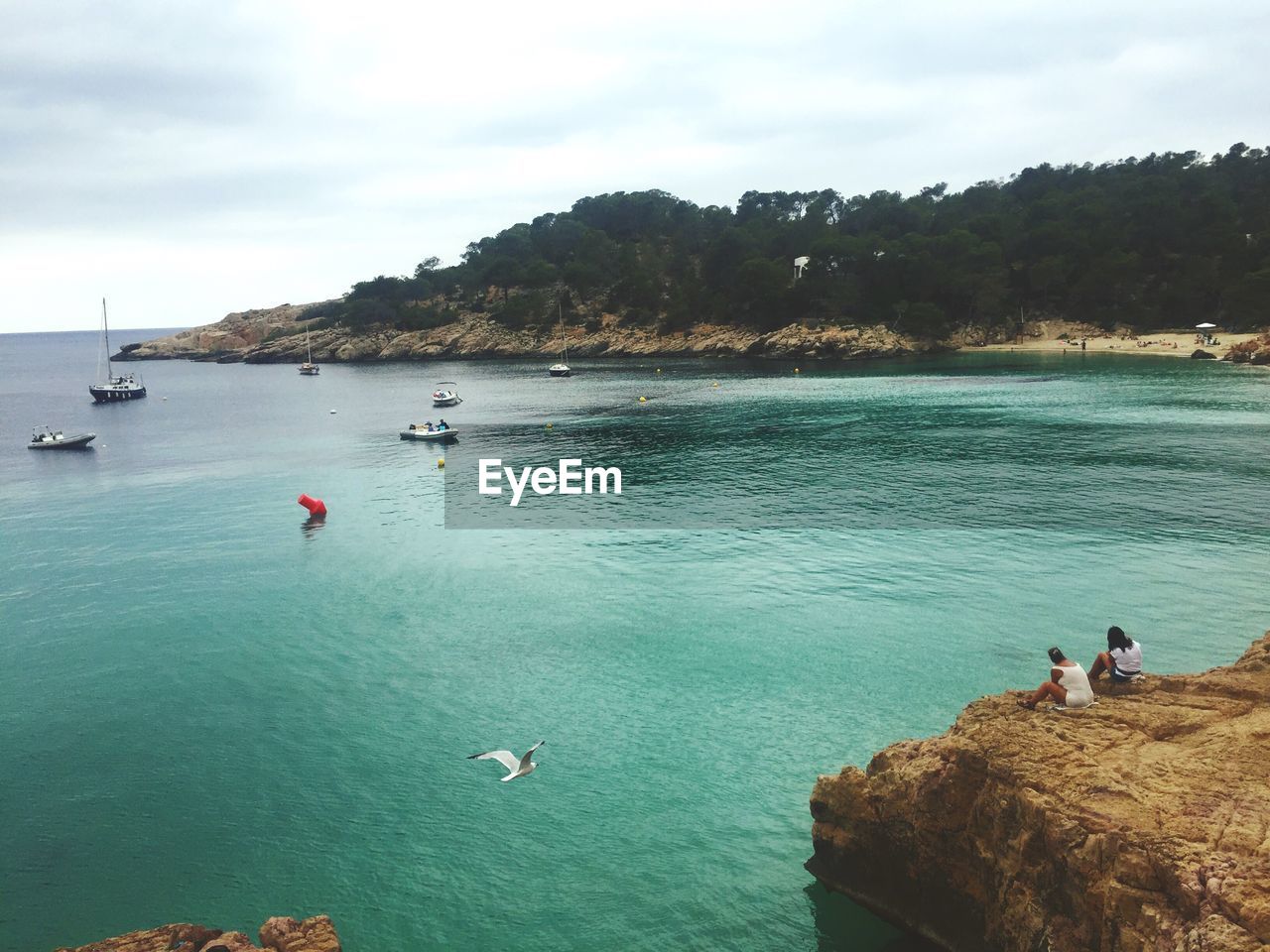 HIGH ANGLE VIEW OF PEOPLE SWIMMING IN SEA BY CLIFF