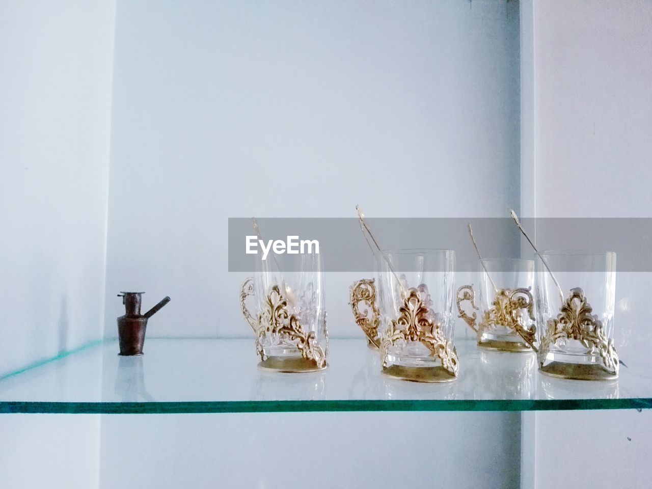 Drinking glasses on glass shelf against wall at home