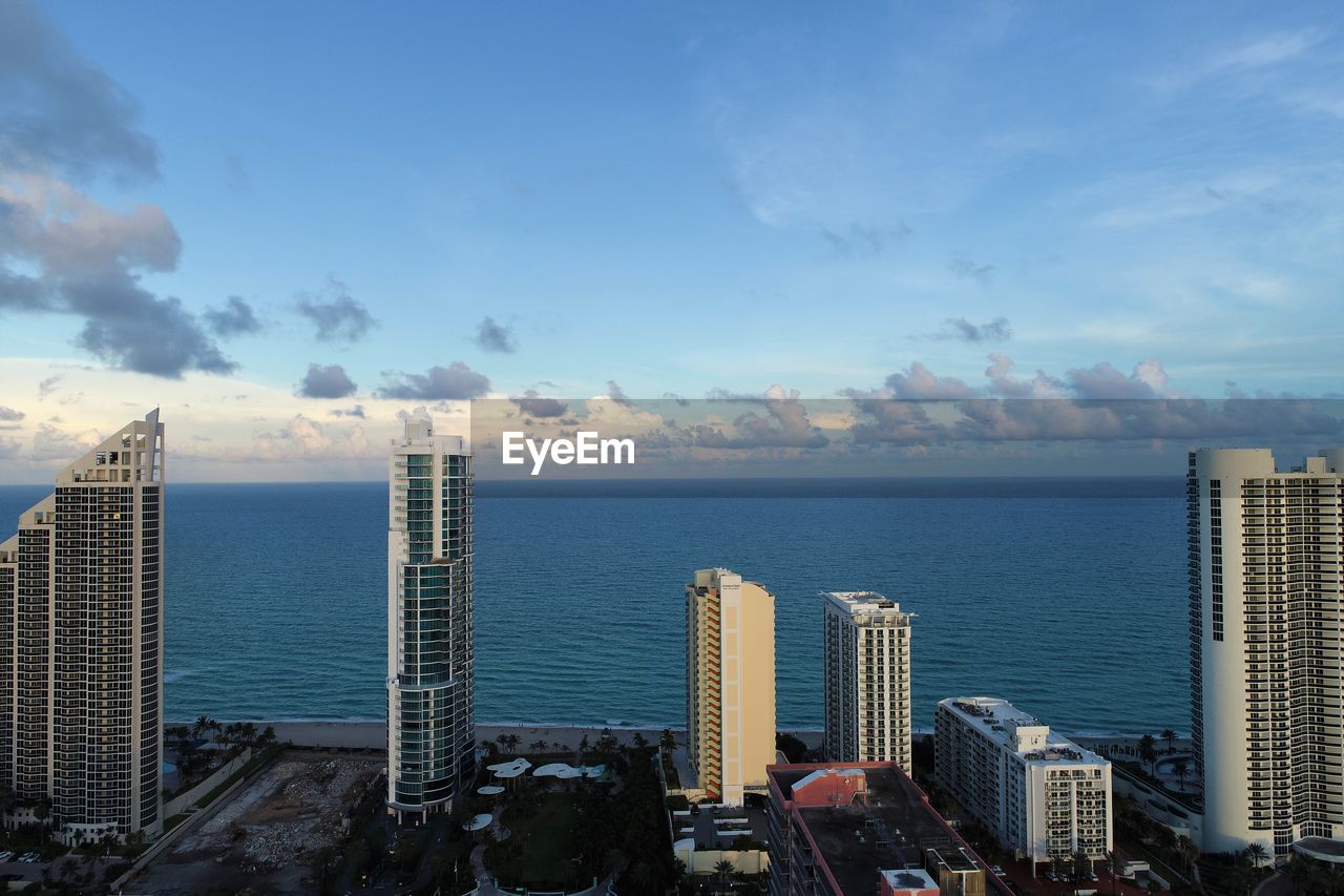 Sea by modern buildings against blue sky