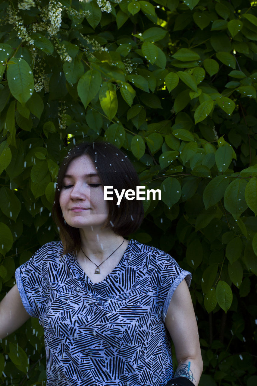 Woman standing with eyes closed against plants during snowfall