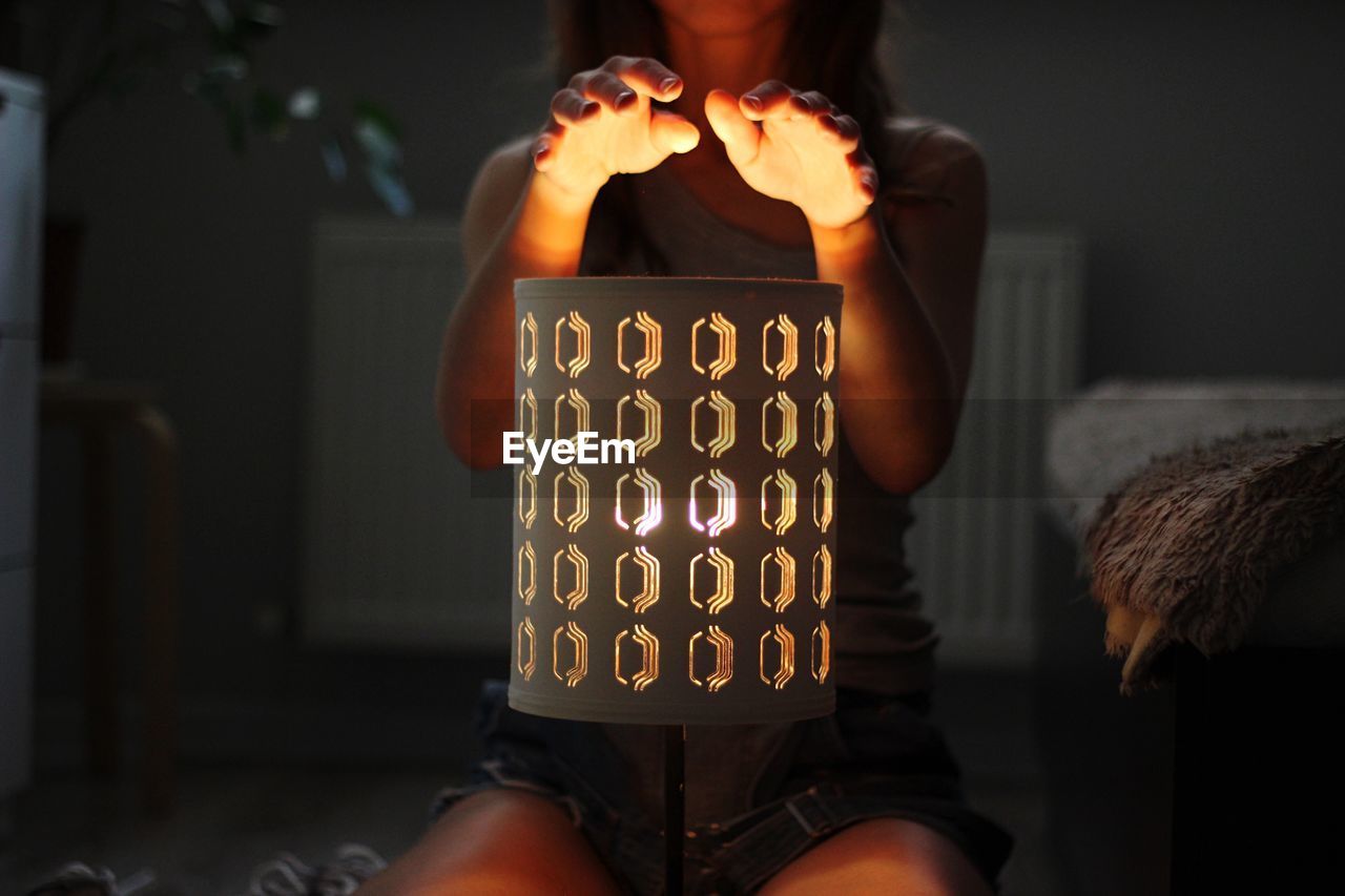 Midsection of woman gesturing over illuminated lantern at home