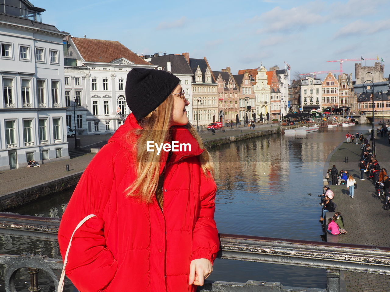 WOMAN STANDING BY CANAL AGAINST CITY