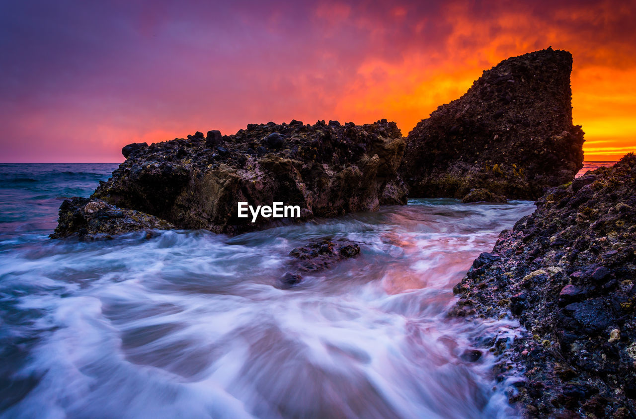 SCENIC VIEW OF ROCKS ON SHORE AGAINST SKY DURING SUNSET