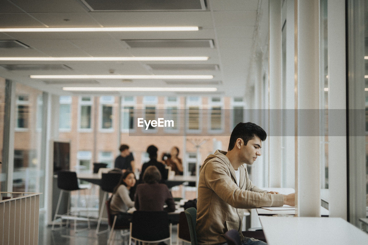 Side view of young student studying at table in university