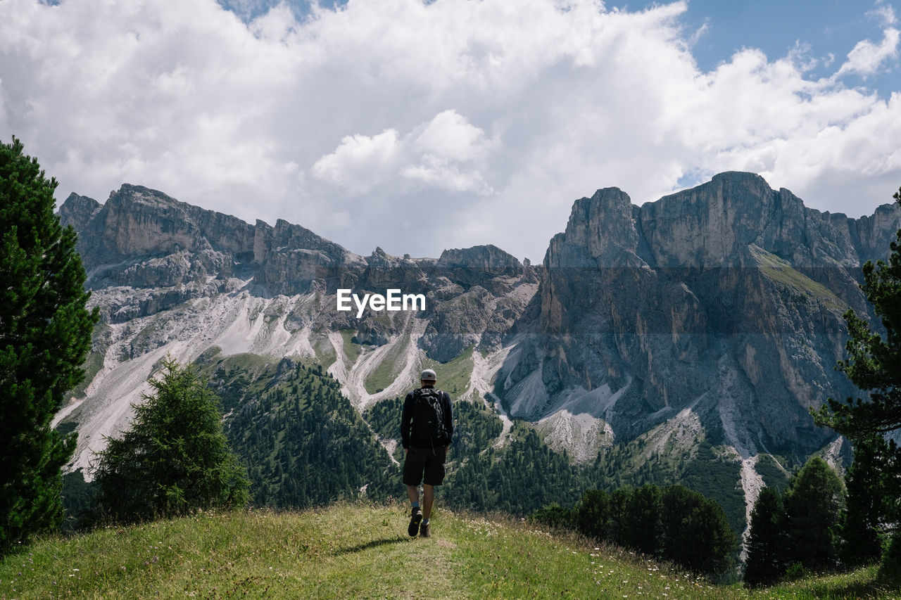 Rear view of hiker walking on mountain against sky