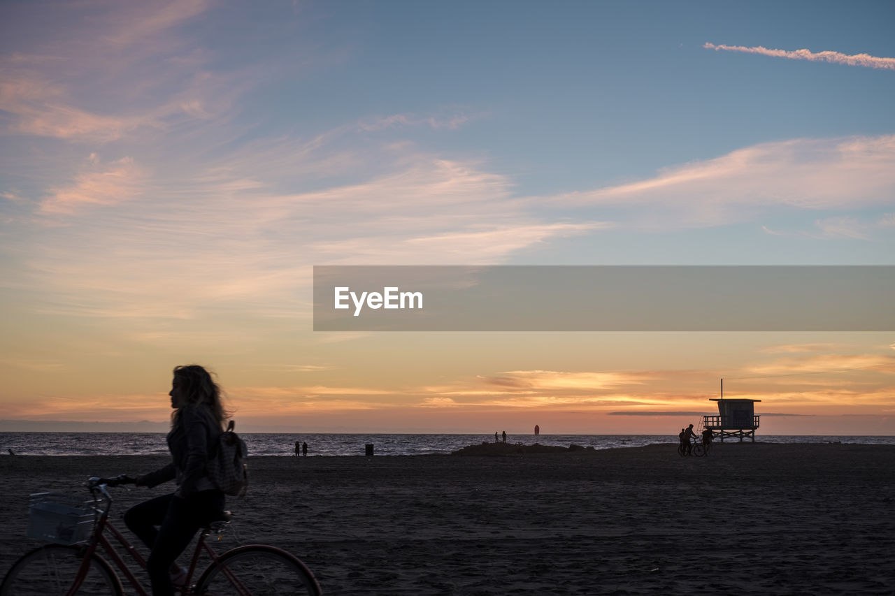 MAN ON BICYCLE BY SEA AGAINST SKY DURING SUNSET