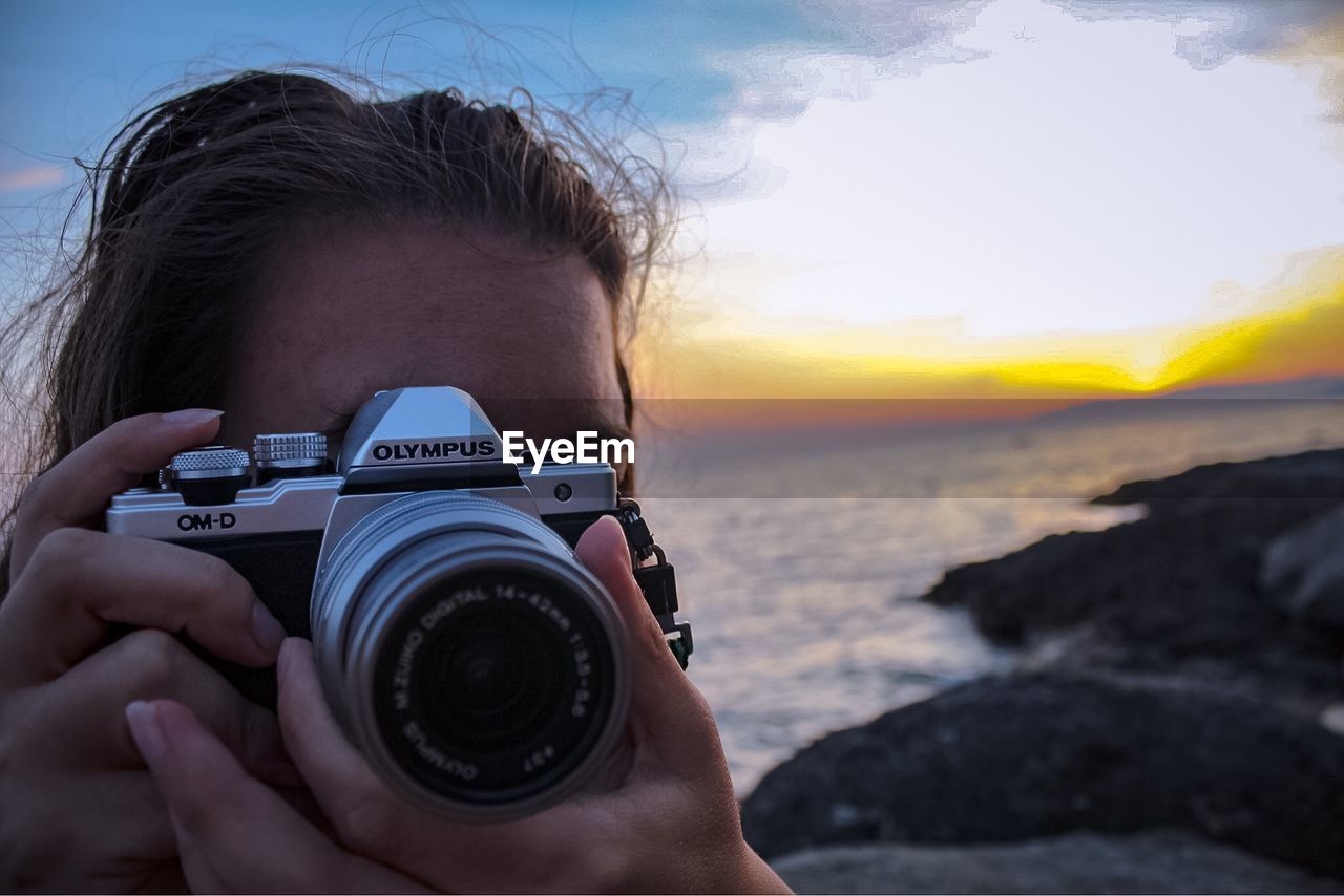 CLOSE-UP OF WOMAN PHOTOGRAPHING SEA AGAINST SKY