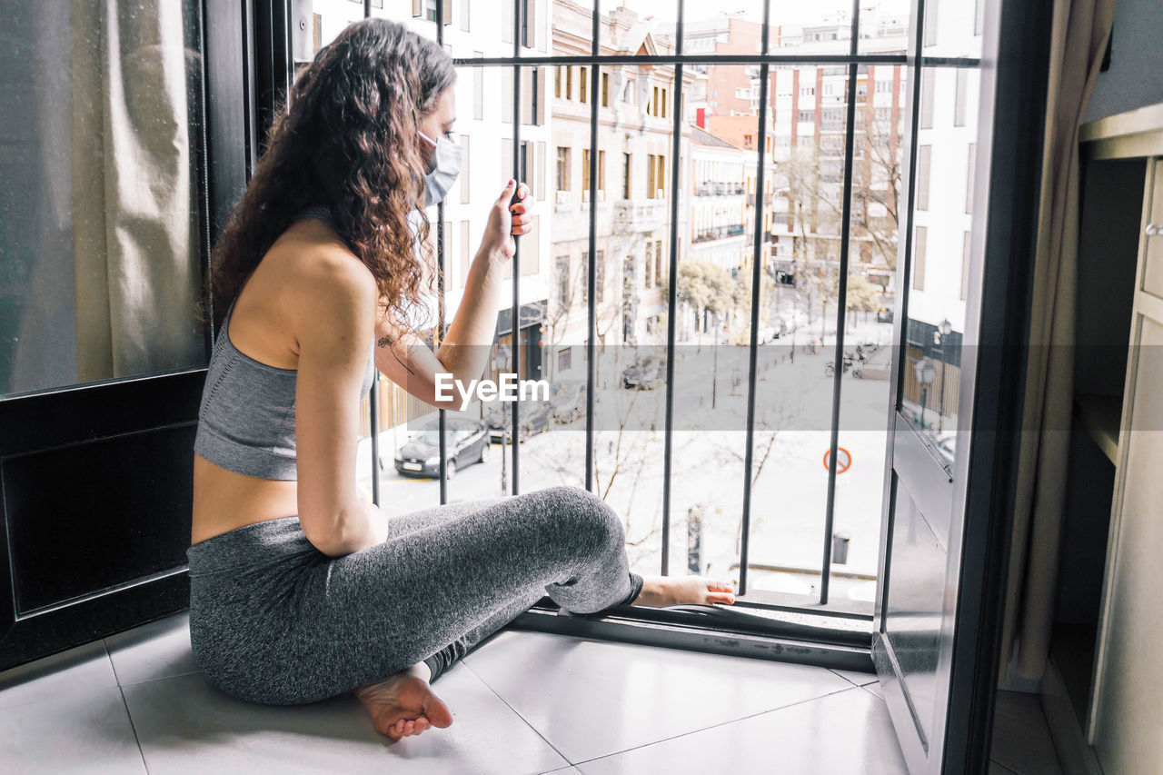 Young girl confinement with face mask at home looking out the window