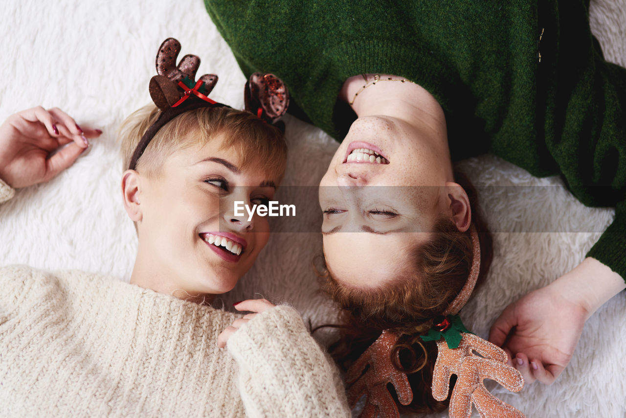 High angle view of cheerful sisters wearing headbands while lying on rug