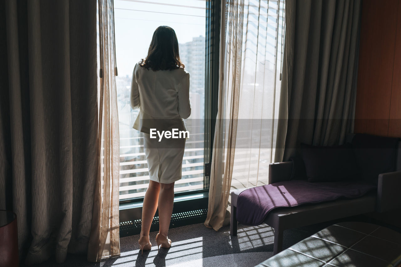 Young brunette woman business lady in white suit in hotel room on high floor