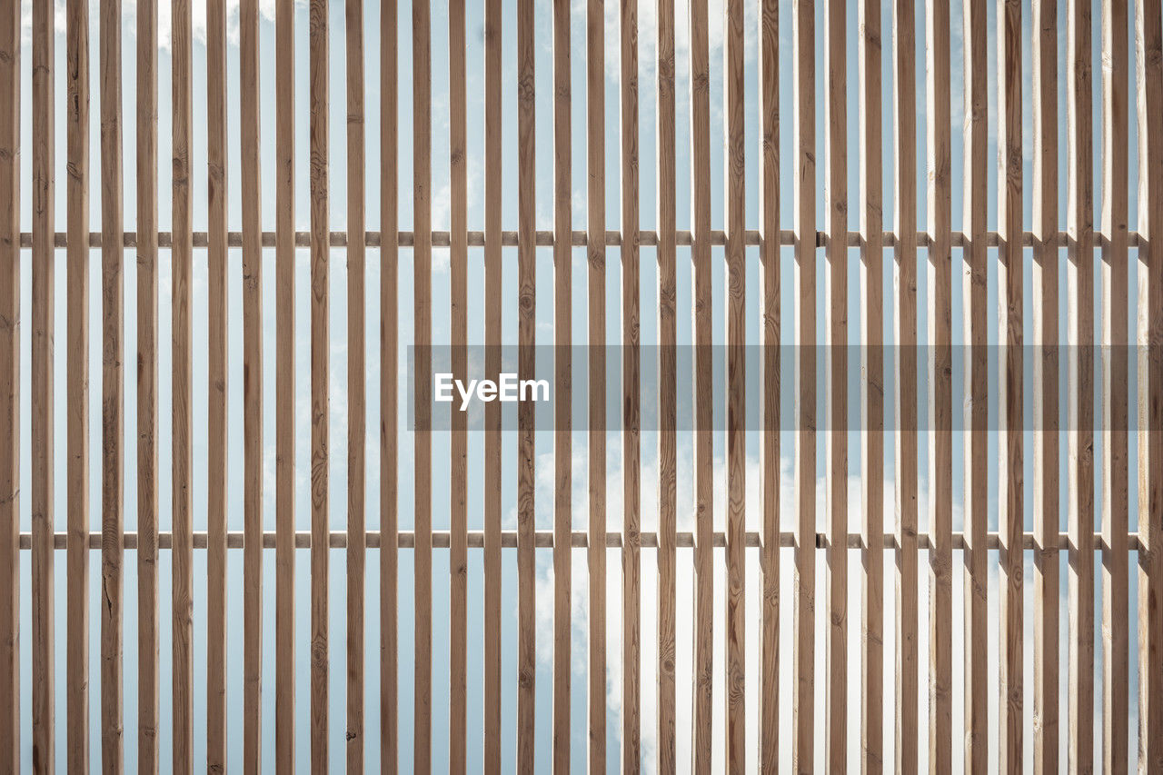 Vertical wooden slats with gaps that reveal the blue sky in the background. 