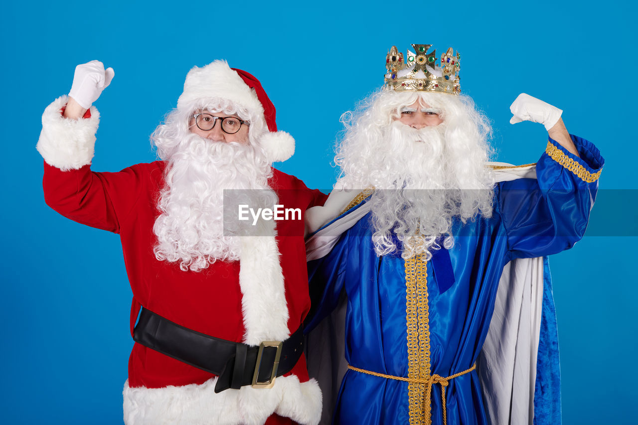 Wise man vs santa claus raising arms on a blue background
