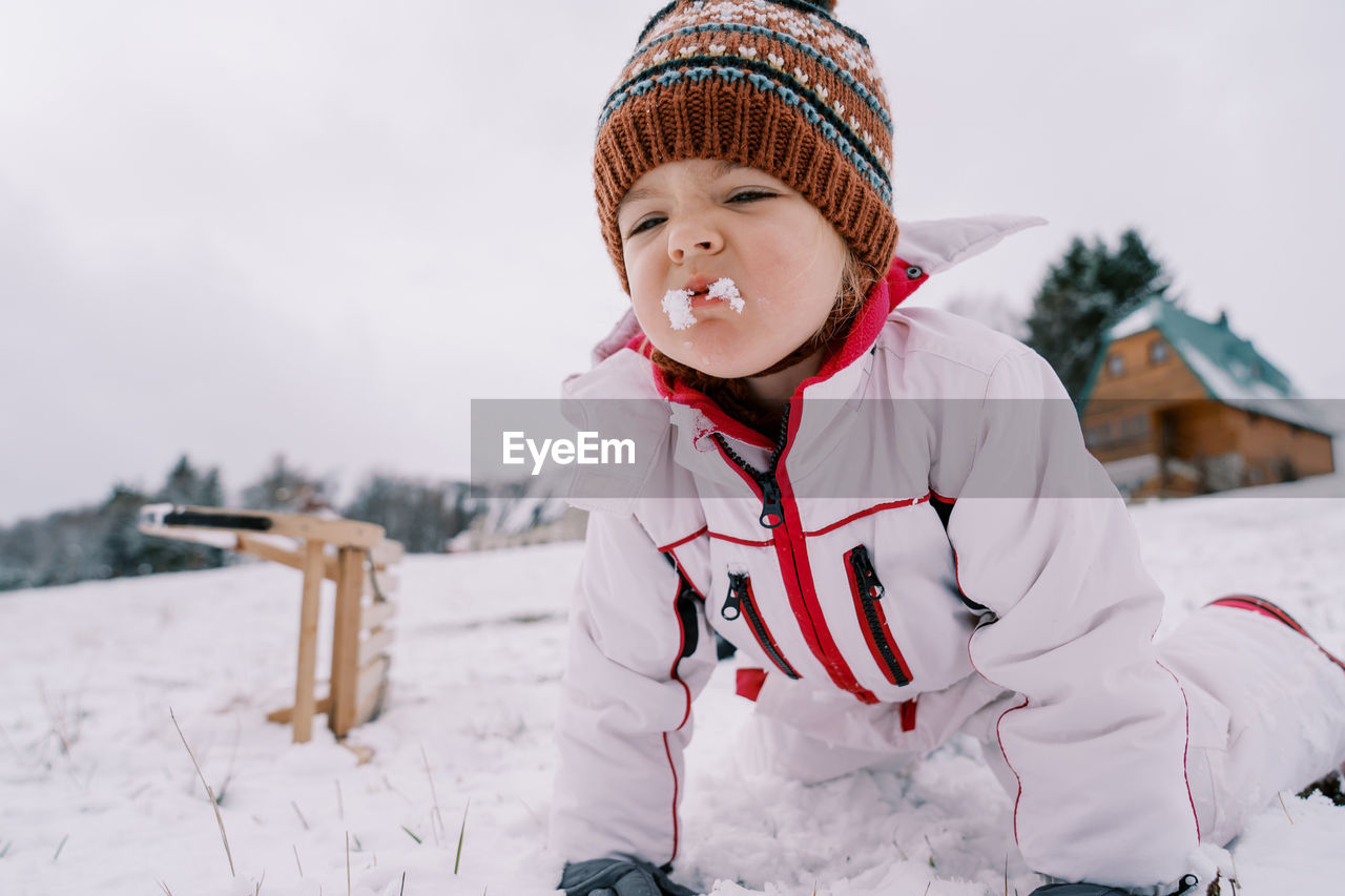 portrait of boy standing on snow covered field against sky