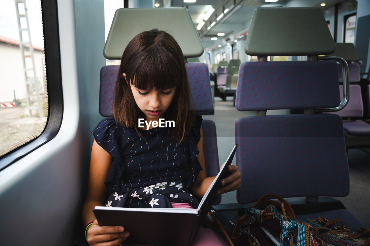 Girl reading book while sitting in train