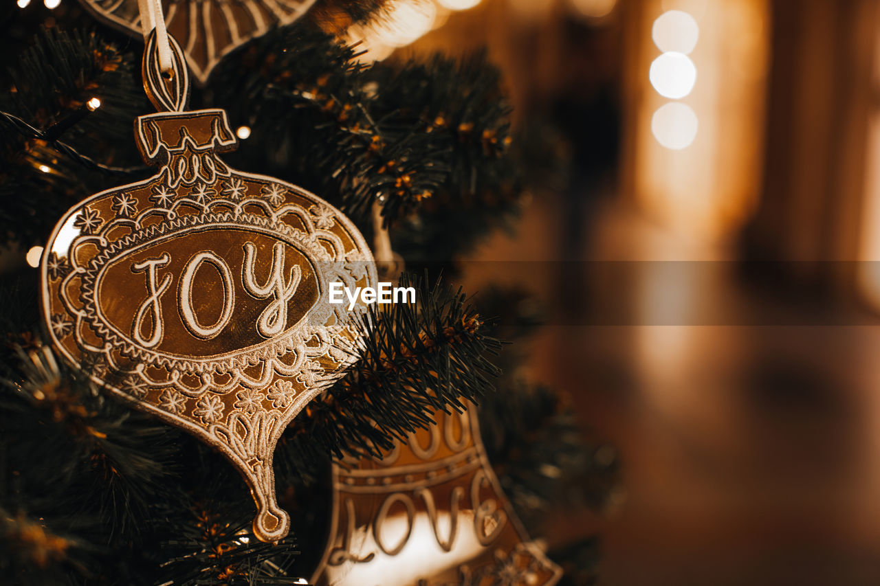 Golden christmas toy with text joy hanging on the tree. golden bokeh lights on festive background