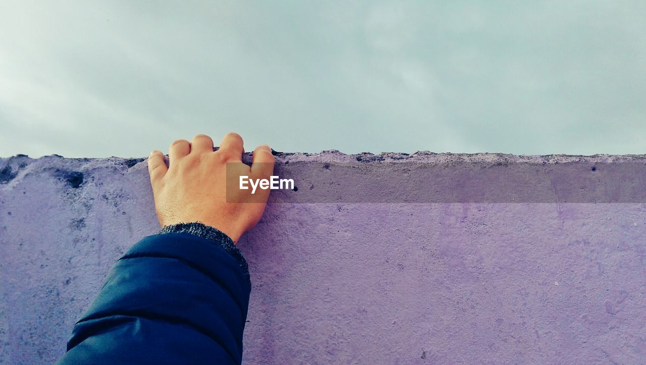 Cropped image of man on purple retaining wall against sky