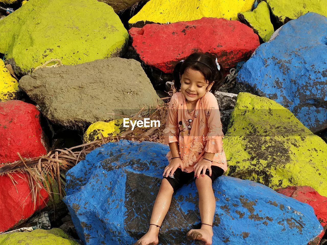 Full length portrait of smiling girl sitting on colorful rocks at beach
