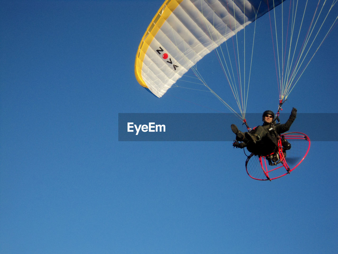 Low angle view of man paragliding against clear blue sky