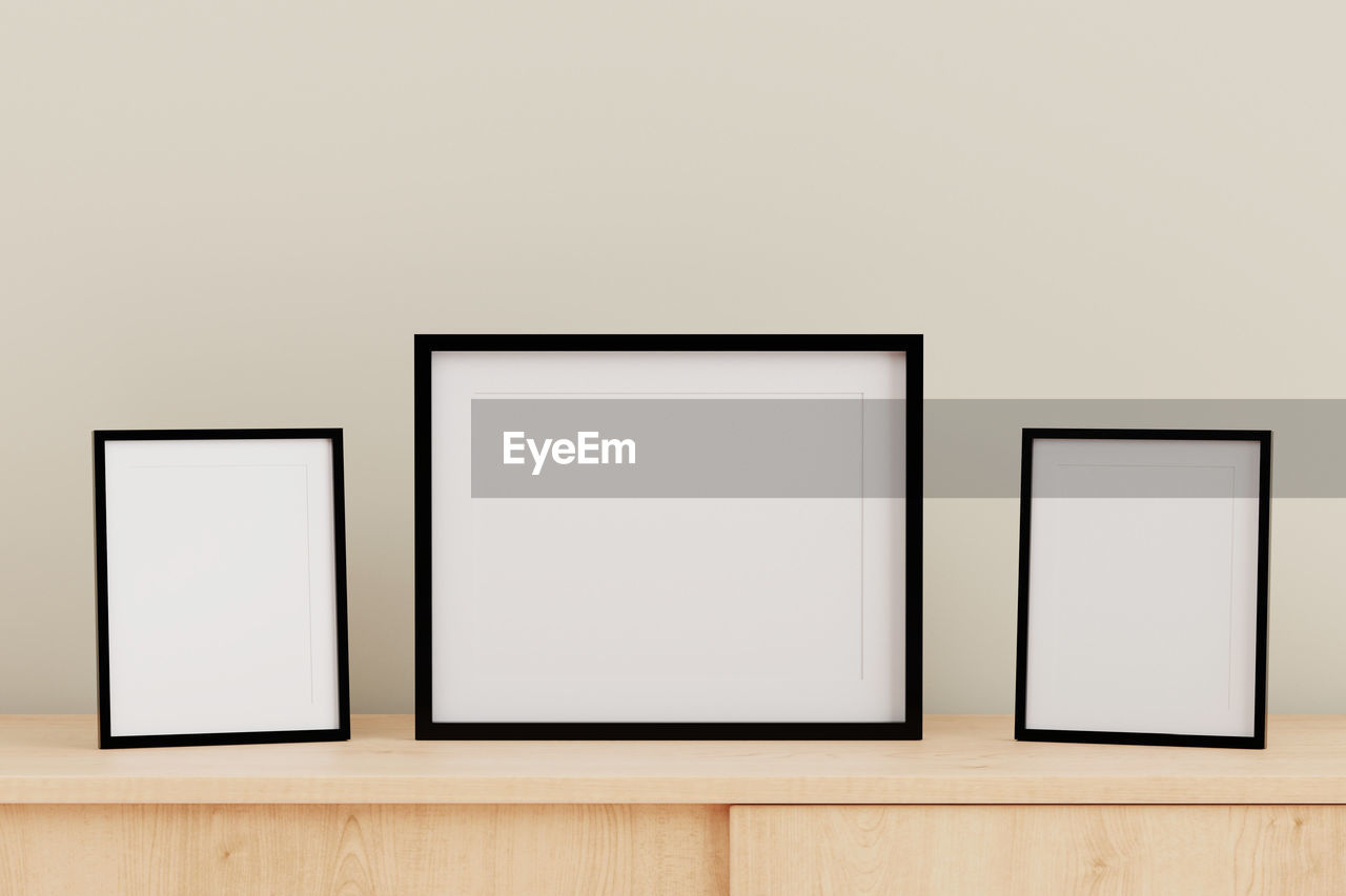 Close-up of blank picture frames on table against gray wall