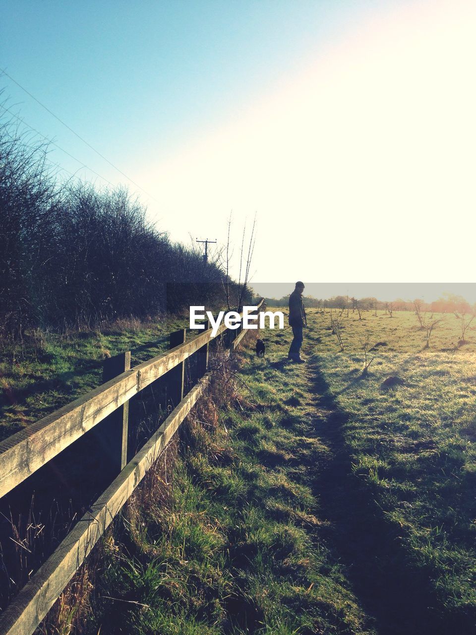 Man standing on grassy field by fence against sky