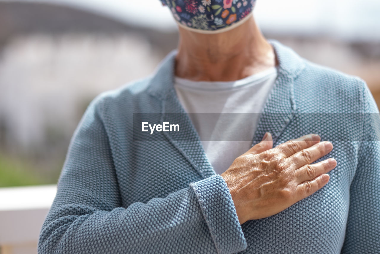 Midsection of senior woman wearing wearing mask gesturing while standing outdoors