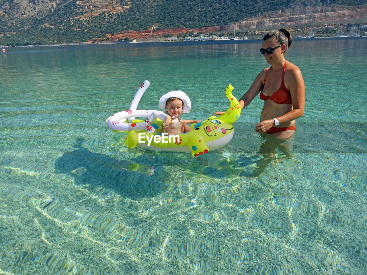 Smiling woman looking at daughter sitting on inflatable ring in sea