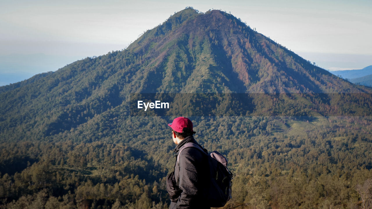 Side view of young man looking at mountain against sky