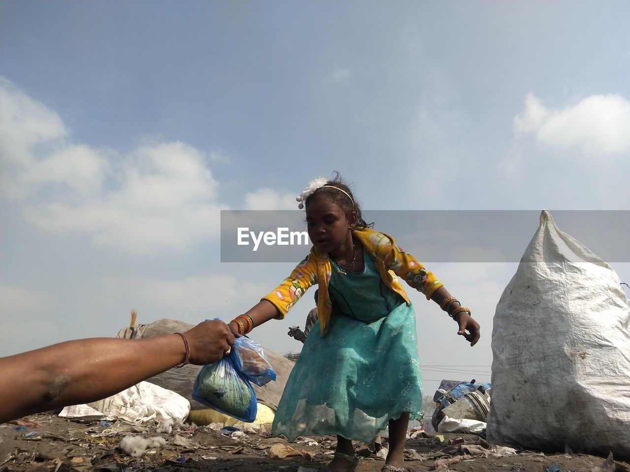 Low angle view of girl with arms raised standing on rock against sky