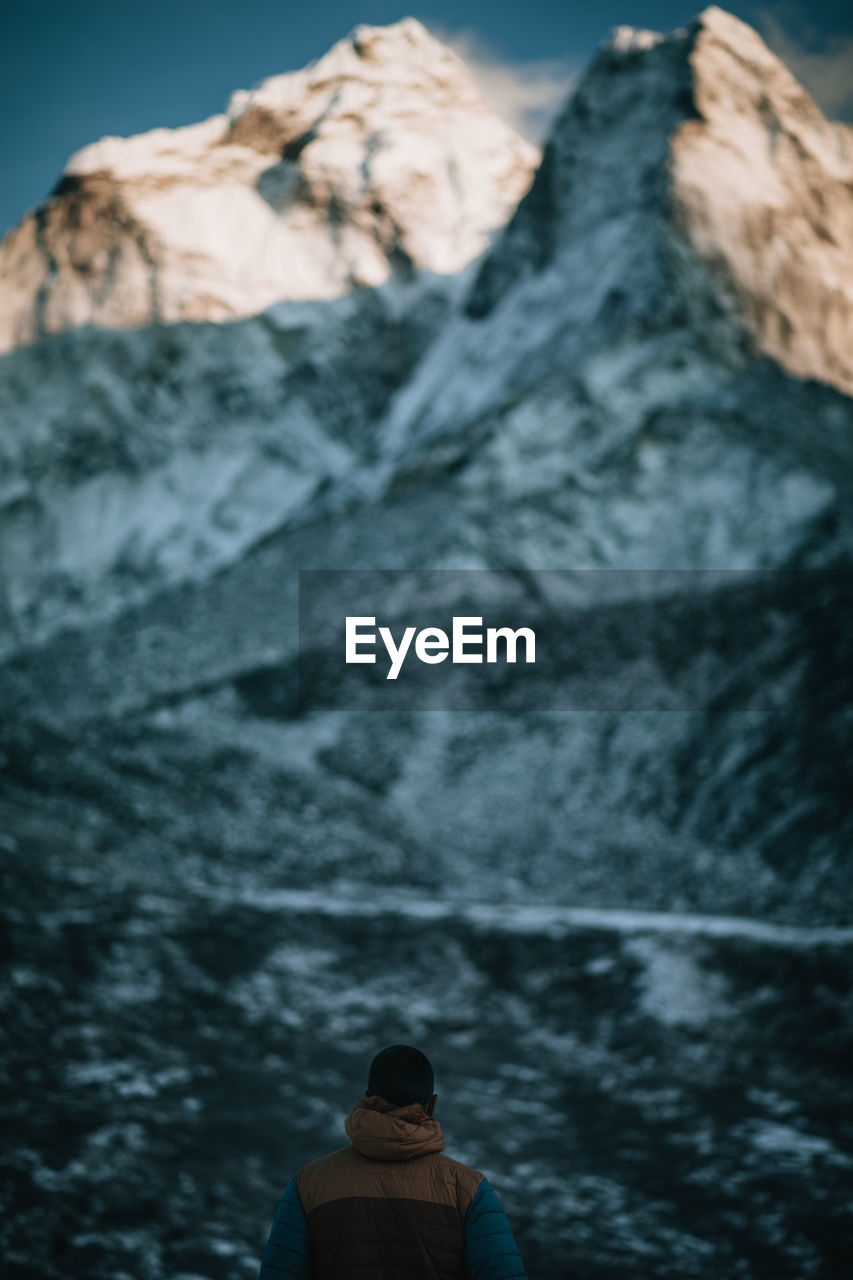 Rear view of man against rocky mountains during winter