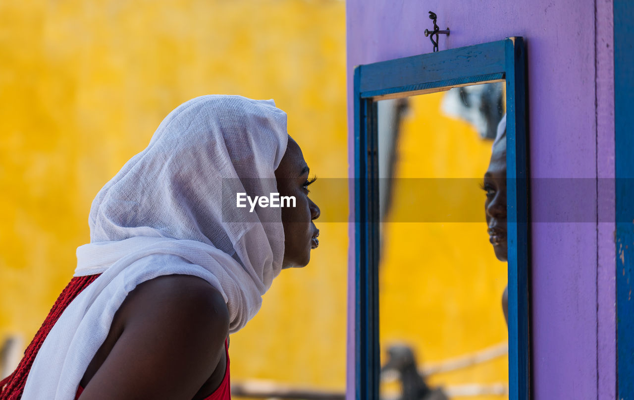 African ghana woman standing in front of a mirror with a white shawl covering her hair