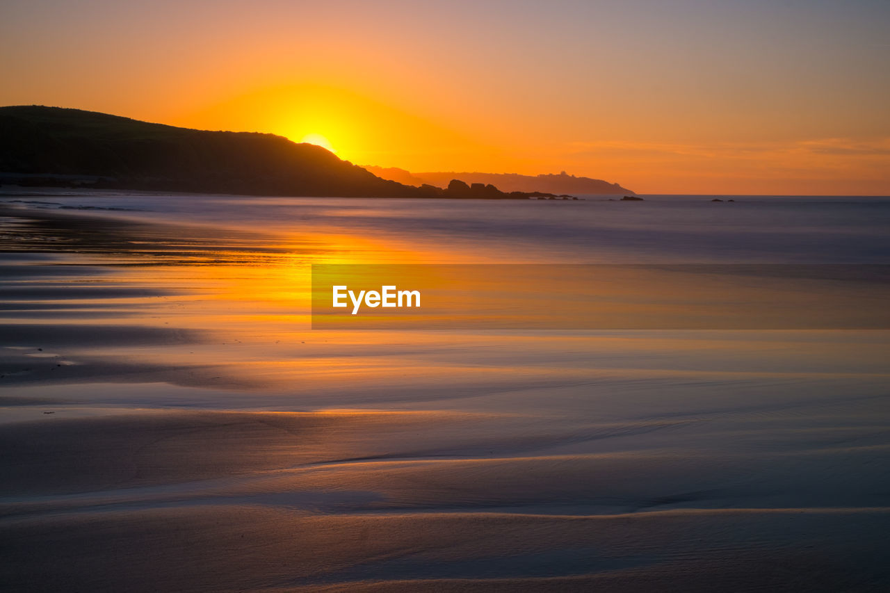 Dreamy sunset light at the beach with orange reflection on wet sand