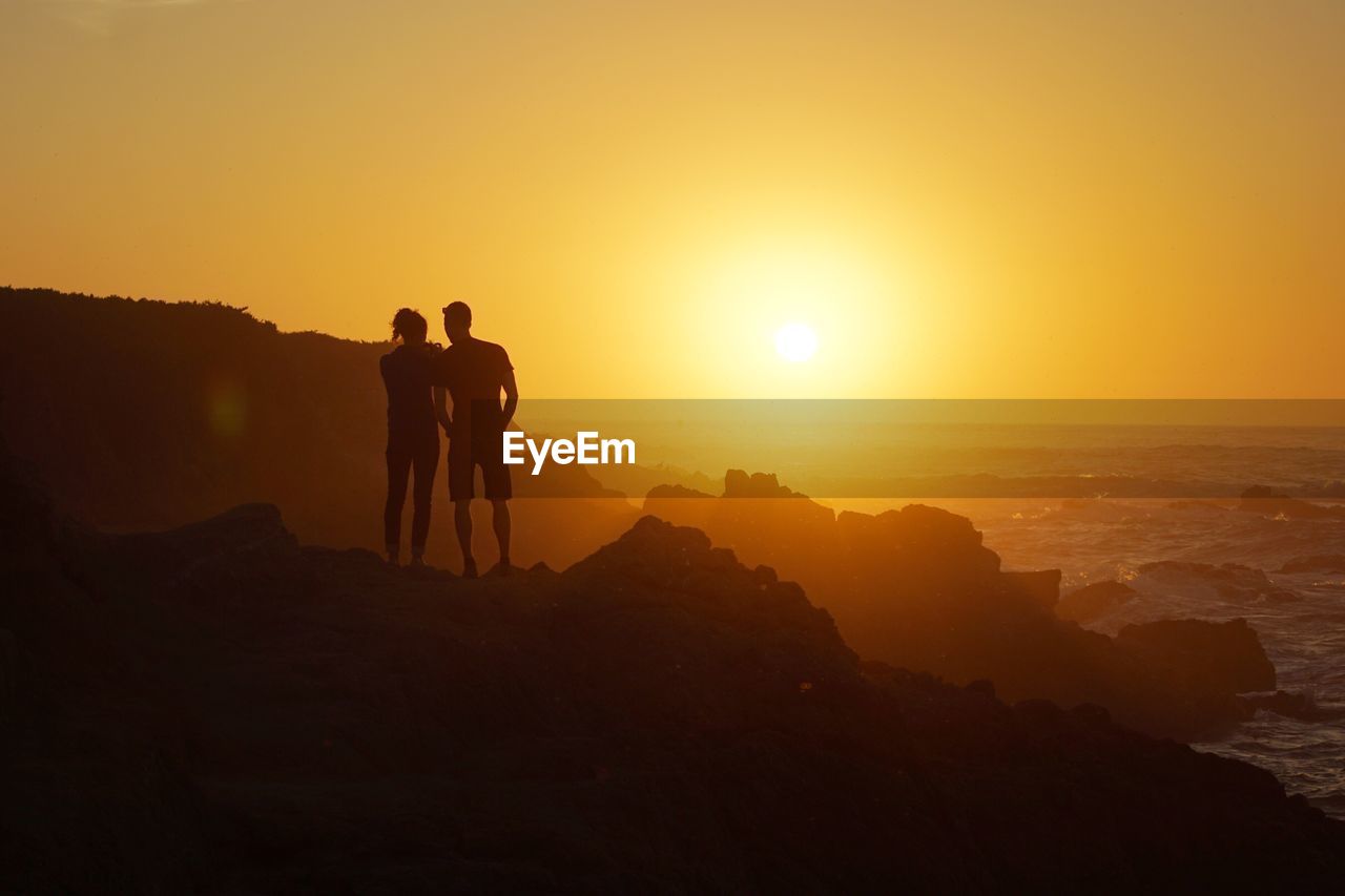 Silhouette people standing by sea against sky during sunset