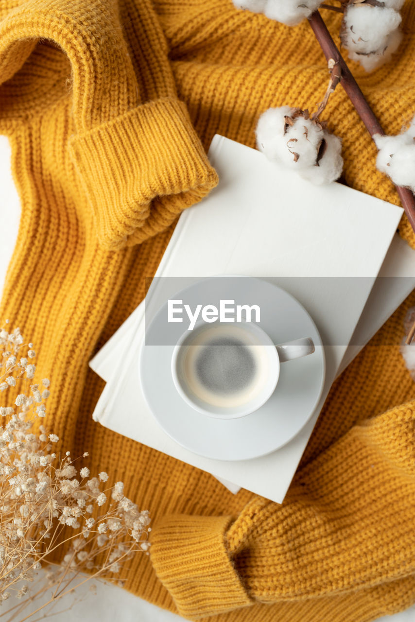 Warm yellow sweater, white books , cup of hot coffee and dry flowers , top view flat lay