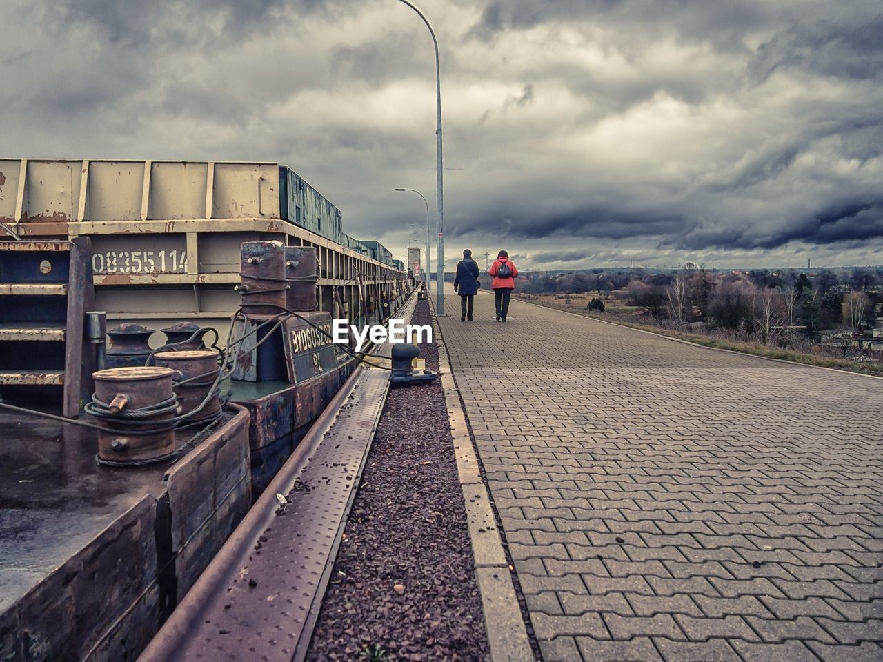 Rear view of people walking by boat moored at harbor