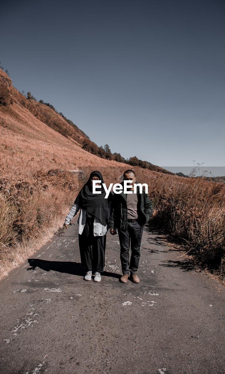 Portrait of couple walking on road against sky