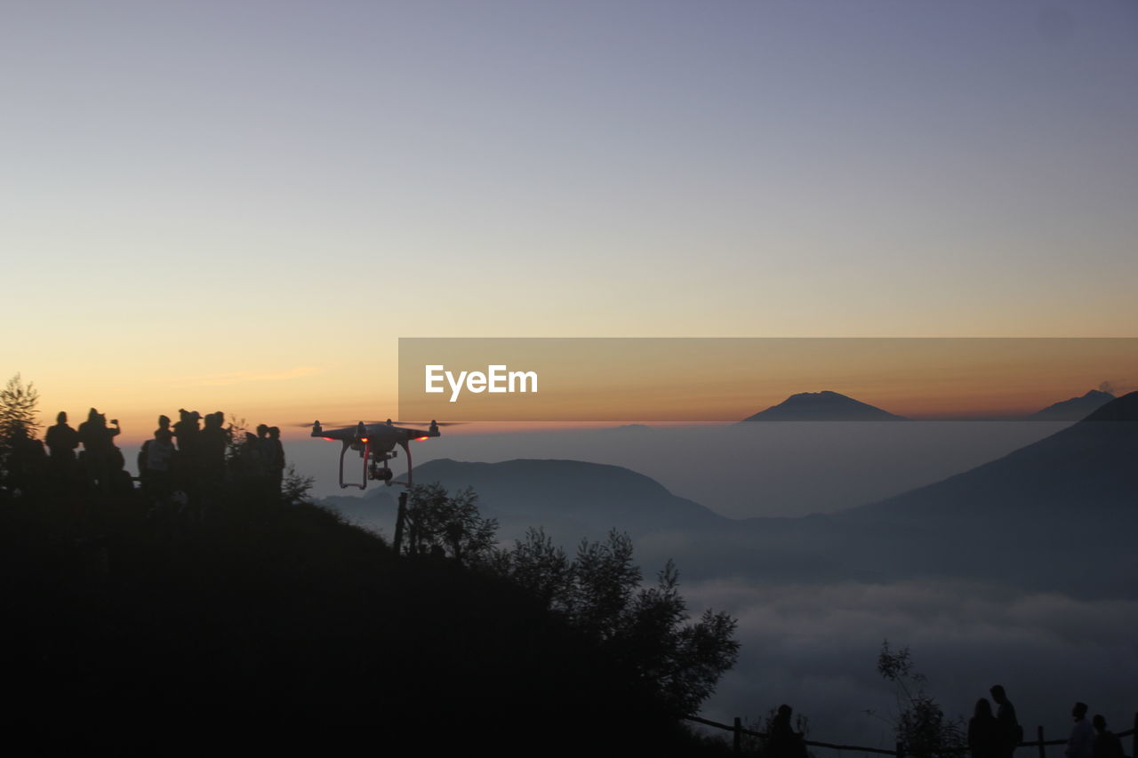 SILHOUETTE PEOPLE ON MOUNTAIN AGAINST ORANGE SKY