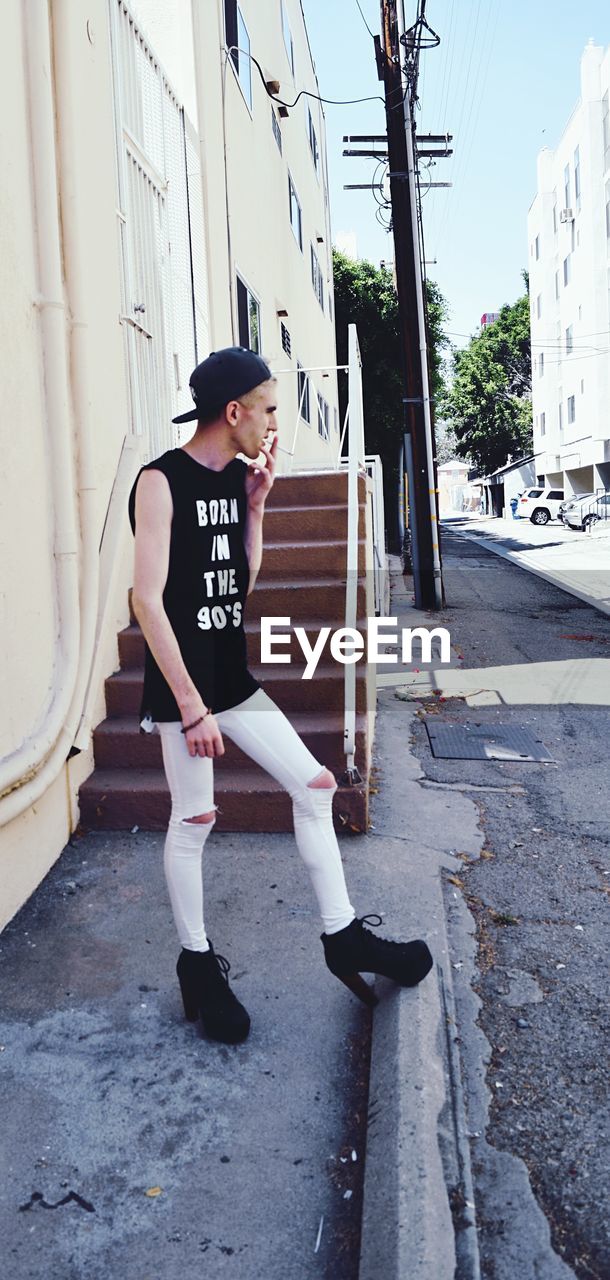 Full length of man in high heels smoking cigarette by road