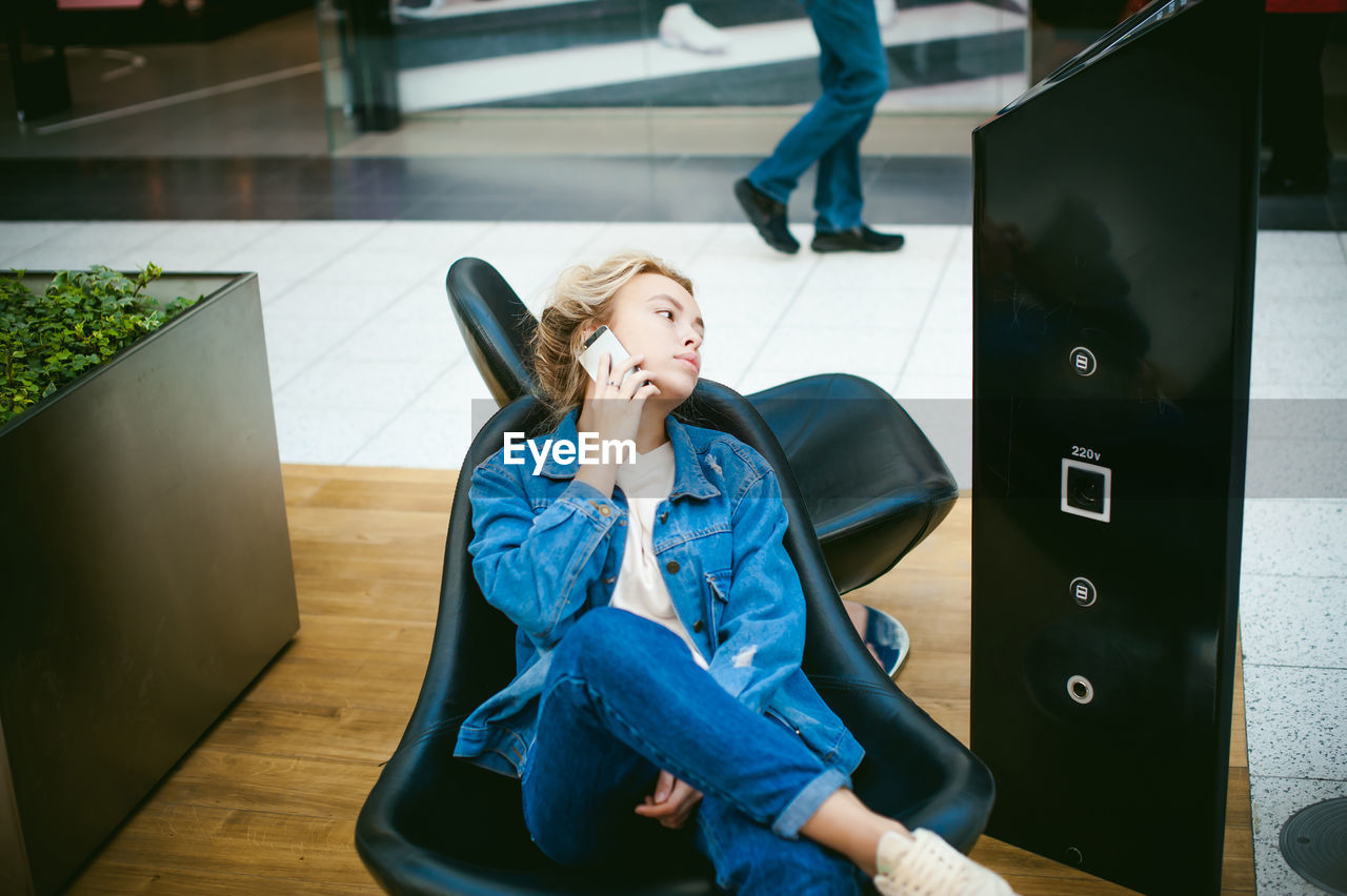 Young woman sitting on chair while talking on mobile phone