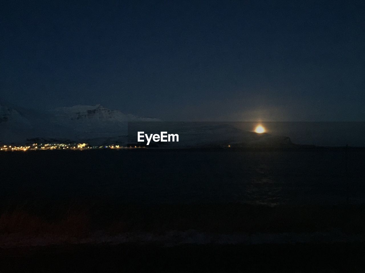 SCENIC VIEW OF ILLUMINATED SEA AGAINST SKY AT NIGHT